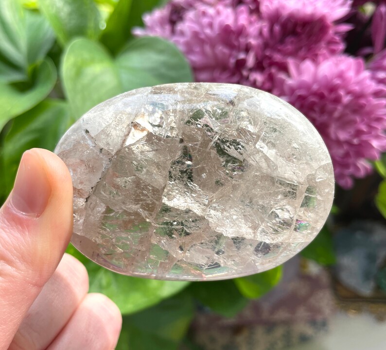 May include: A clear, oval-shaped crystal with a unique, fractured, and iridescent appearance. The crystal has a smooth, polished surface and is a natural gemstone.