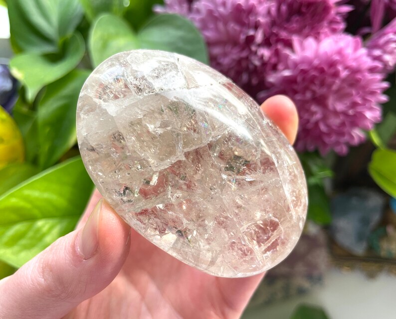 May include: A clear quartz crystal palm stone with a unique, textured surface. The crystal is smooth and polished, with a slightly oval shape.