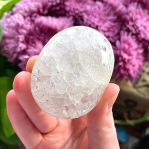 May include: A clear, white, oval-shaped crystal with a textured surface. The crystal is about the size of a golf ball.