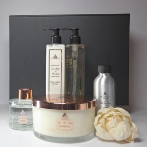 May include: A gift set featuring a white candle, a clear glass bottle of diffuser oil, a silver bottle of diffuser refill, and two bottles of hand and body lotion. The bottles are labelled "Lime Basil & Mandarin" and "White Rose & Oud". The gift set is presented against a black backdrop.