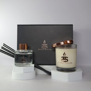 Puede incluir: Una caja de regalo negra con una vela blanca y una botella de difusor. Tanto la vela como la botella de difusor tienen una tapa de cobre y un logotipo que dice "Simple Scents".