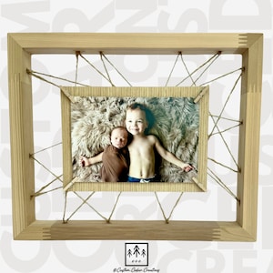 May include: A wooden picture frame with a photo of two brothers. The frame is made of natural wood and has a rustic look. The photo shows a young boy holding a baby. The frame is decorated with twine and has a small wooden sign with the text "Custom Cedar Creations" at the bottom.
