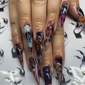 May include: Close-up of long, pointed, stiletto nails with a variety of colorful designs. The nails are decorated with images of a Starbucks logo, a cartoon character, and other abstract patterns.