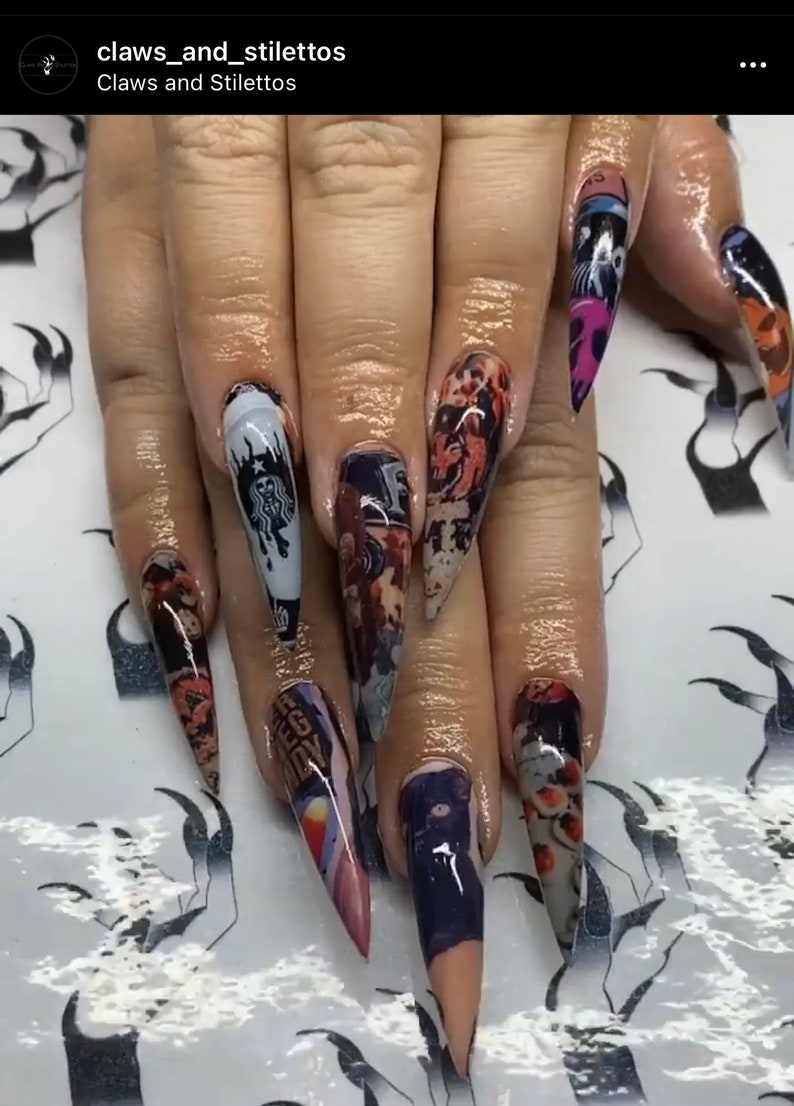 May include: Close-up of long, pointed, stiletto nails with a variety of colorful designs. The nails are decorated with images of a Starbucks logo, a cartoon character, and other abstract patterns.