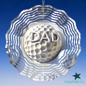 May include: A silver metal wind chime with a golf ball design and the word "DAD" on it. The wind chime has a circular shape with multiple layers of wavy lines.