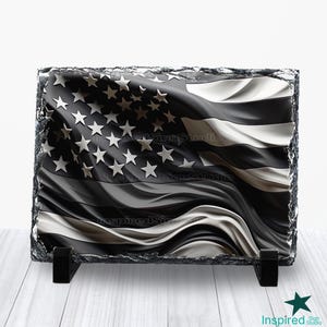 Könnte beinhalten: Schwarz-weiße amerikanische Flagge auf einer Schiefertafel mit Ständer gedruckt. Die Flagge weht im Wind.