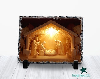 May include: A rectangular, illuminated nativity scene carved into a dark stone. The scene depicts Mary, Joseph, and baby Jesus in a manger, with sheep and other figures. The light shines from behind the figures, creating a warm glow.