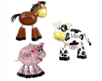 May include: Three hanging ornaments shaped like a brown horse with the name Gray, a black and white cow with the name Mia, and a pink pig with the name Staci. Each animal figure features dangling legs and the word year printed on the lower parts.