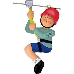 May include: A personalized Christmas ornament featuring a cartoon person ziplining. The person is wearing a blue shirt, blue shorts, a red helmet, and black shoes. The ornament is inscribed with the name "Jeff" and the year.