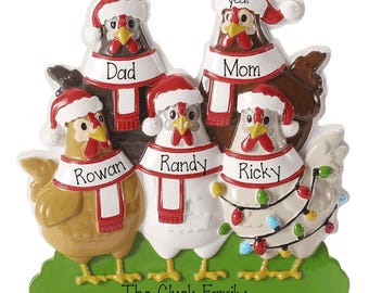 May include: A decorative ornament featuring five chickens standing on a green base. Each chicken wears a red and white Santa hat and a scarf. The scarves are labeled with the names Dad, Mom, Rowan, Randy, and Ricky. The base reads The Cluck Family.