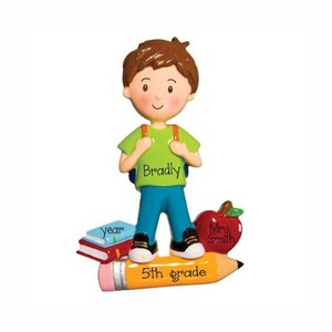 May include: Personalized Christmas ornament featuring a boy standing on a pencil with a book, apple, and the text "5th grade" and "Mrs. Smith". The boy is wearing a green shirt with the name "Bradly" on it.