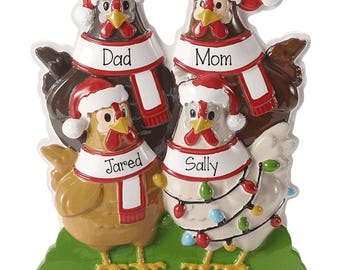 May include: A decorative ornament featuring four chickens standing on a green base. Each chicken wears a red and white Santa hat and a scarf labeled with the names Dad, Mom, Jared, and Sally. The white chicken is wrapped in colorful Christmas lights.