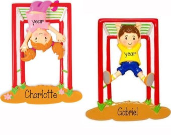 May include: Two hanging ornaments featuring children on monkey bars. One ornament shows a girl in a pink shirt with the text year and Charlotte. The other shows a boy in a yellow shirt with the text year and Gabriel. Both have red frames.