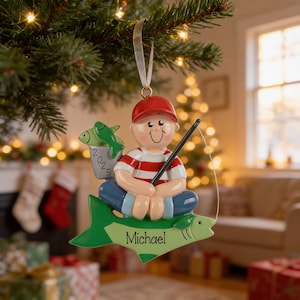 A personalized ornament hanging from a Christmas tree, featuring a smiling boy in a red hat and striped shirt, holding a fishing rod and accompanied by a fish.