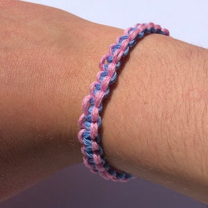 Puede incluir: Un brazalete de amistad rosa y azul hecho con cuerda trenzada.