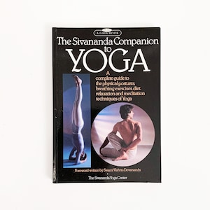 May include: A black book with a white title that reads "The Sivananda Companion to YOGA". The book cover features two people in yoga poses, one in a headstand and the other in a seated pose. The book cover also includes the text "A complete guide to the physical postures, breathing exercises, diet, relaxation and meditation techniques of Yoga".