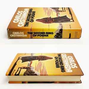 May include: A yellow and orange paperback book with the title "The Second Ring of Power" by Carlos Castaneda. The cover features a person wearing a brown robe walking on a path with mountains in the background.