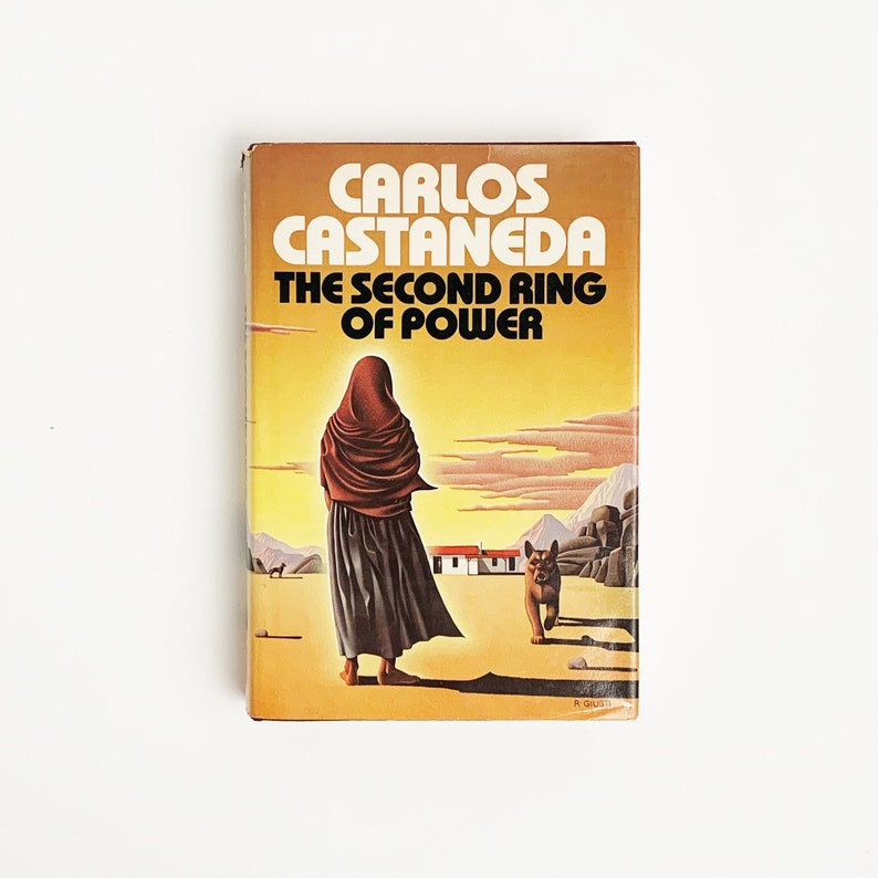 May include: A yellow, orange, and brown paperback book with the title "Carlos Castaneda The Second Ring of Power" on the cover. The cover features a woman in a brown robe and a dog in the background.