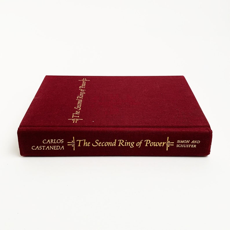 May include: A burgundy hardcover book with gold lettering on the spine and front cover. The title is "The Second Ring of Power" by Carlos Castaneda. The book is published by Simon and Schuster.