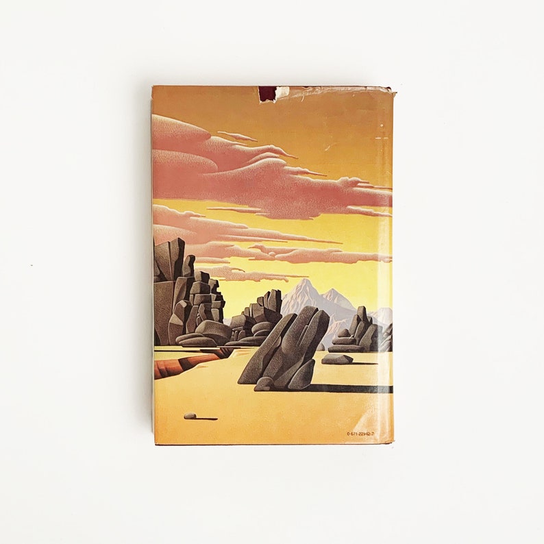 May include: A vintage paperback book cover with an illustration of a rocky landscape under a sunset sky. The sky is a gradient of pink, orange, and yellow. The rocks are brown and gray. The book cover has a yellow background with a red stripe at the top.