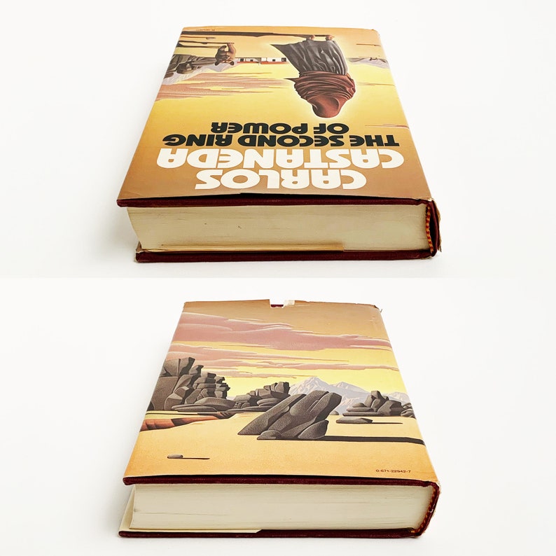 May include: A vintage paperback book with a yellow cover and red spine. The cover features a desert landscape with a figure in the distance. The title of the book is "Carlos Castaneda The Second Ring of Power".