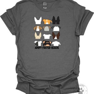 May include: A dark gray short-sleeve t-shirt featuring a graphic of twelve dog heads in a grid pattern with various coat colors and ear shapes. Below the dogs, the text ADOPT-FOSTER-RESCUE is printed in black capital letters with small paw prints.