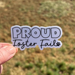 Peut inclure: Autocollant blanc avec du texte noir qui dit "Proud Foster Fail" avec une empreinte de patte.