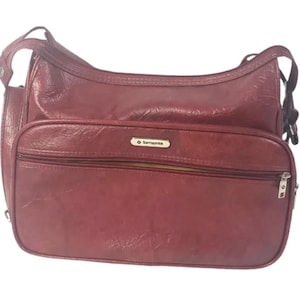 Pode incluir: Uma bolsa de viagem de couro bordô com um bolso com zíper e o logotipo da Samsonite.