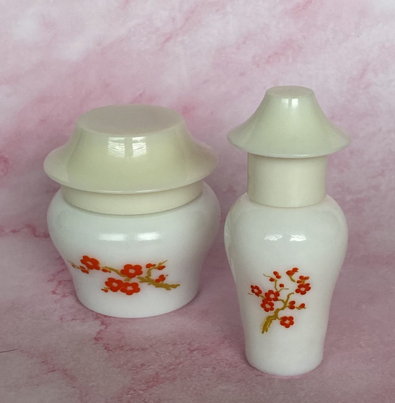 Puede incluir: Dos tarros de cer&aacute;mica blancos con tapas blanquecinas. Cada tarro presenta una rama de flores rojas con tallos dorados. Los tarros tienen una est&eacute;tica vintage y probablemente sean decorativos o para almacenamiento.