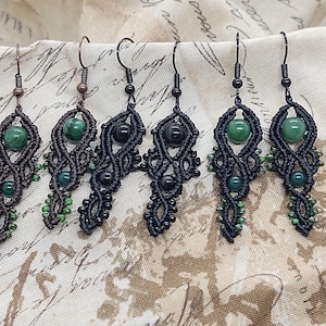 May include: Five pairs of handmade macrame earrings with green and black beads. The earrings are made with black cord and feature a variety of green stones.