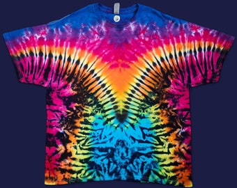 Puede incluir: Una camiseta tie-dye con un patrón de arcoíris y remolinos negros. La camiseta tiene cuello en V y mangas cortas.