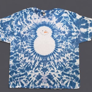 Puede incluir: Una camiseta azul y blanca tie-dye con una cara de muñeco de nieve blanca en el centro.