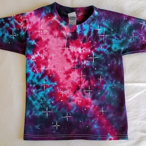 Puede incluir: Una camiseta tie-dye en tonos de rosa, azul y morado con brillantes blancos en forma de estrella.
