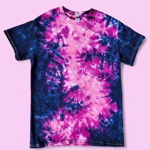 Puede incluir: Una camiseta tie-dye con un patrón de espiral rosa y azul. La camiseta está hecha de un material suave y cómodo y es perfecta para el uso casual.