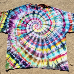 Puede incluir: Una camiseta tie-dye con un patrón de espiral colorido en tonos de azul, verde, amarillo, rojo, morado y negro.