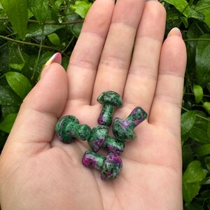 May include: A collection of six small green and pink gemstone mushroom carvings. The mushrooms are polished and have a smooth, rounded surface.