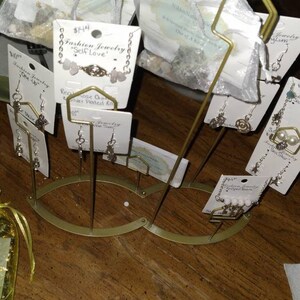 May include: A gold metal stand with multiple tiers holding various jewelry pieces. The jewelry includes earrings, a necklace, and a bracelet. The jewelry is displayed on small white cards with text that reads "Fashion Jewelry "Self Love" and "Rose Quartz Silver Plated Ring".