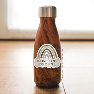 May include: A brown water bottle with a sticker that says "Raise Kind Humans" and features a rainbow with a cloud.