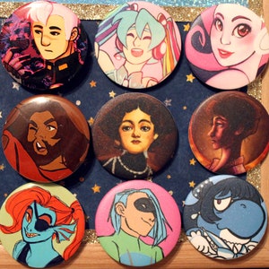 May include: Nine round pinback buttons with various colorful designs. The buttons feature a variety of characters, including a person with blue hair, a person with brown hair, a person with pink hair, a person with green hair, a person with black hair, a person with blue skin, and a person with white skin. The buttons are all different sizes and shapes.