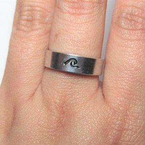 Peut inclure: Une bague en argent avec un motif de vague gravé sur la bande.