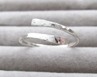May include: A silver ring with a hammered texture. The ring has an open design, with two ends that overlap. The ring is set against a grey background.