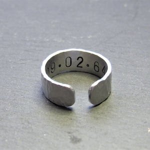 May include: A silver ring with a hammered finish and the inscription "19.02.64" engraved on the band.
