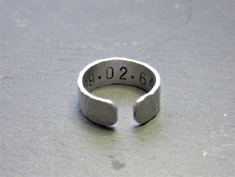 May include: A silver ring with a hammered finish and the inscription "19.02.64" engraved on the band.