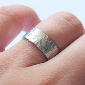 May include: A silver hammered band ring worn on a finger.