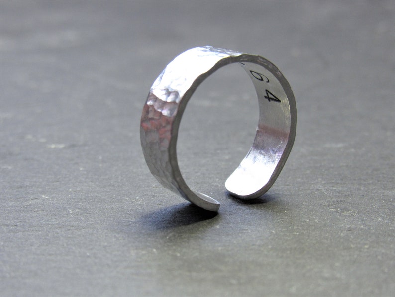 May include: A silver hammered metal ring with a split band and the number "64" engraved on the side.