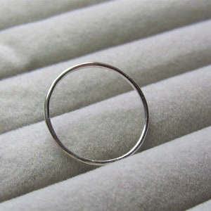 May include: A simple silver ring, shown on a grey textured surface.