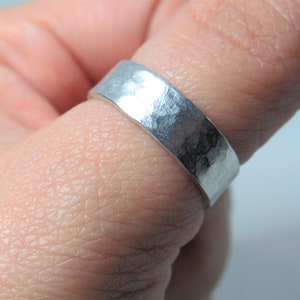 May include: A silver hammered band ring worn on a finger.