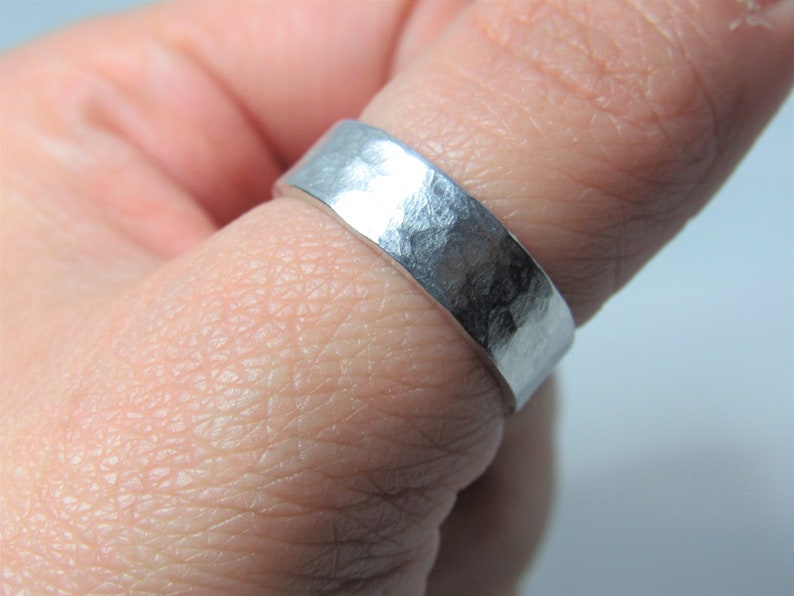 May include: A silver hammered band ring worn on a finger.