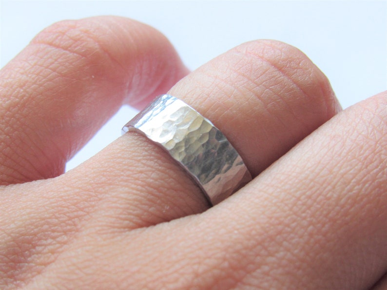 May include: A silver hammered band ring worn on a finger.