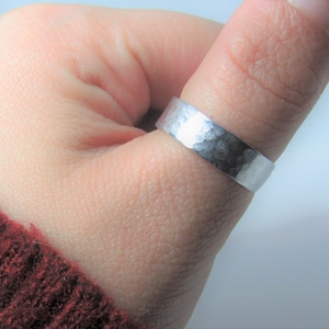 May include: A silver hammered ring worn on a finger.